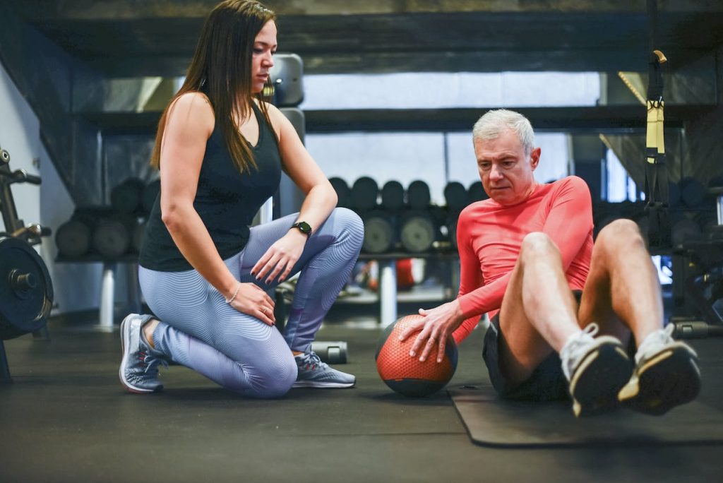 Man in Red Shirt Doing Shoulder Exercise Beside a Woman in Black Tank Top