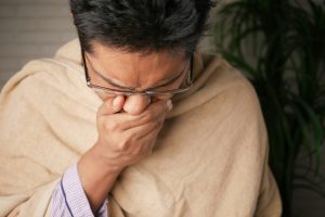 man wrapped in a blanket, coughing