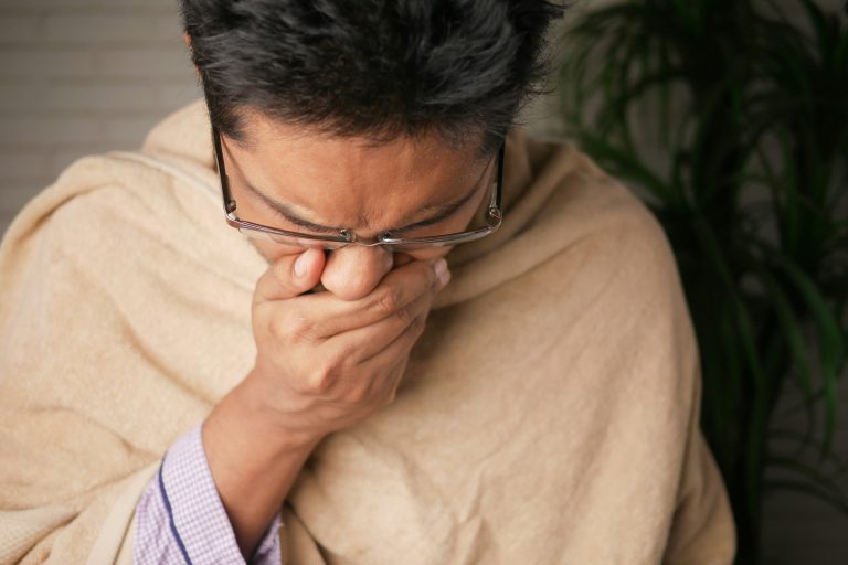 man wrapped in a blanket, coughing